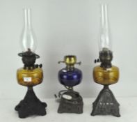 Three Victorian oil lamps, on scrolling metal supports, one with a blue glass reservoir,