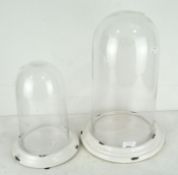 Two glass clock domes on white glazed ceramic stands, 20th century, 40 cm high max.