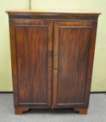 An early 20th century mahogany cupboard with two shelves behind double doors raised on shaped feet,