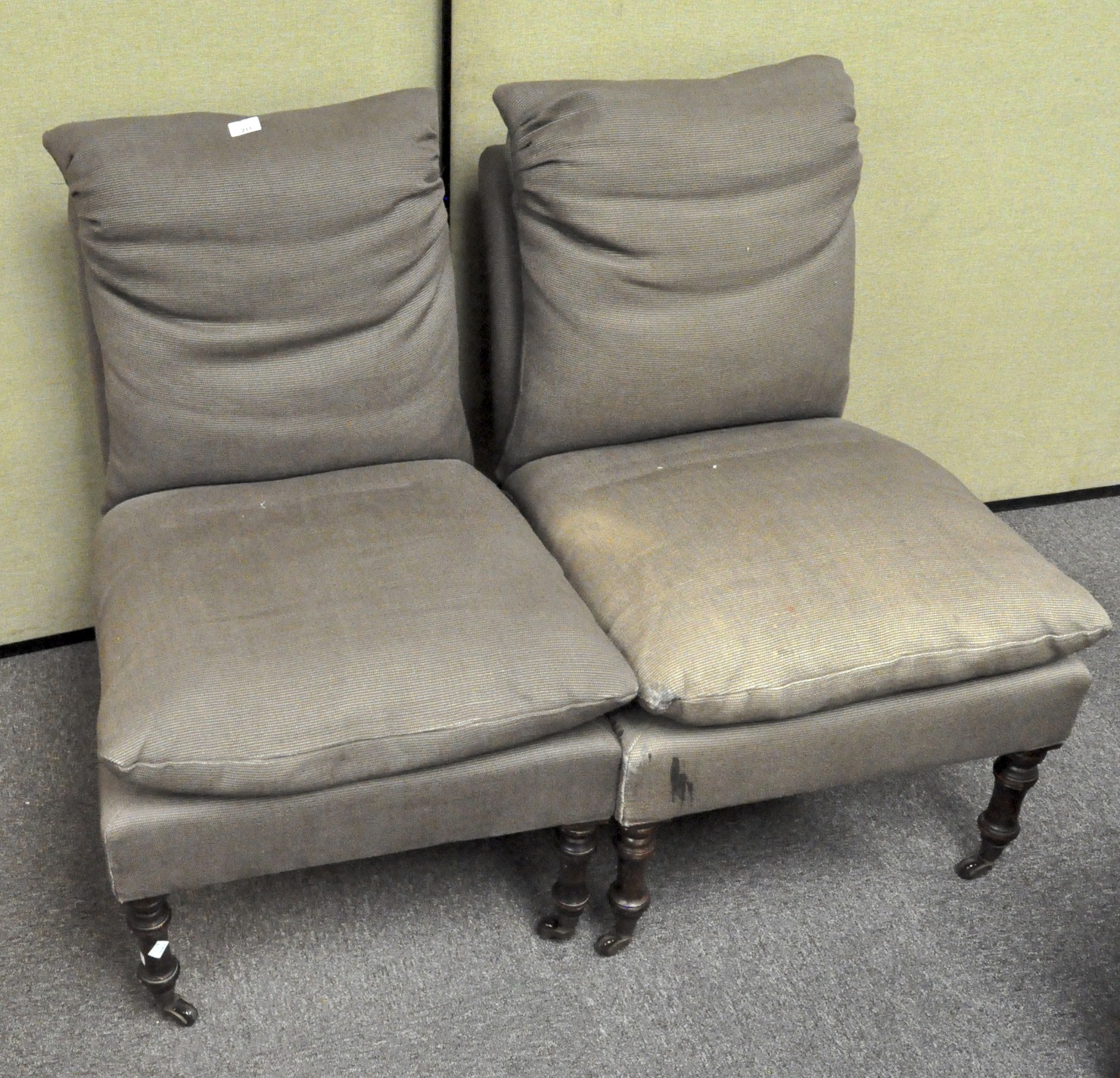 Two grey upholstered chairs, each with cushion backs and seats, on casters,