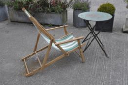 A deck chair with striped fabric and a green painted metal garden table,