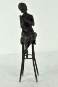A bronze figure depicting a lady in Art Deco dress, perched upon a stool,