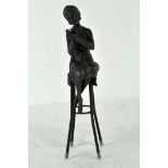 A bronze figure depicting a lady in Art Deco dress, perched upon a stool,