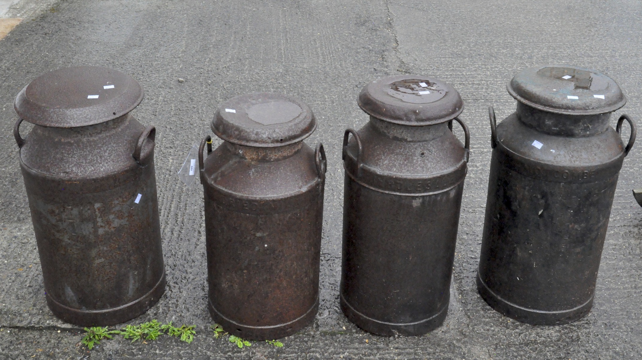 A group of four cast metal milk churns, with lids and handles to either side,