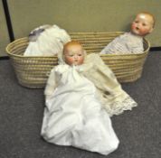 A vintage wicker basket containing three German (Armand Marseille) bisque dolls,