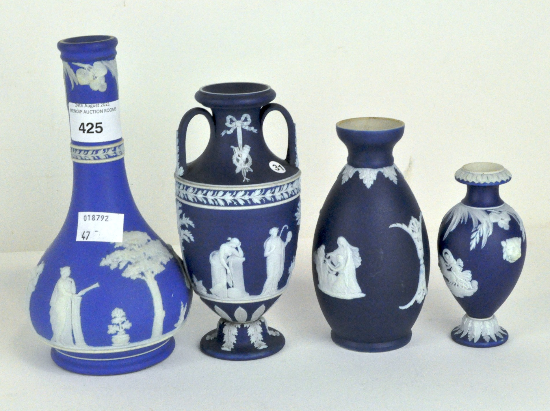 Four Wedgwood blue jasperware vases of varying shapes and decorated with classical motifs,