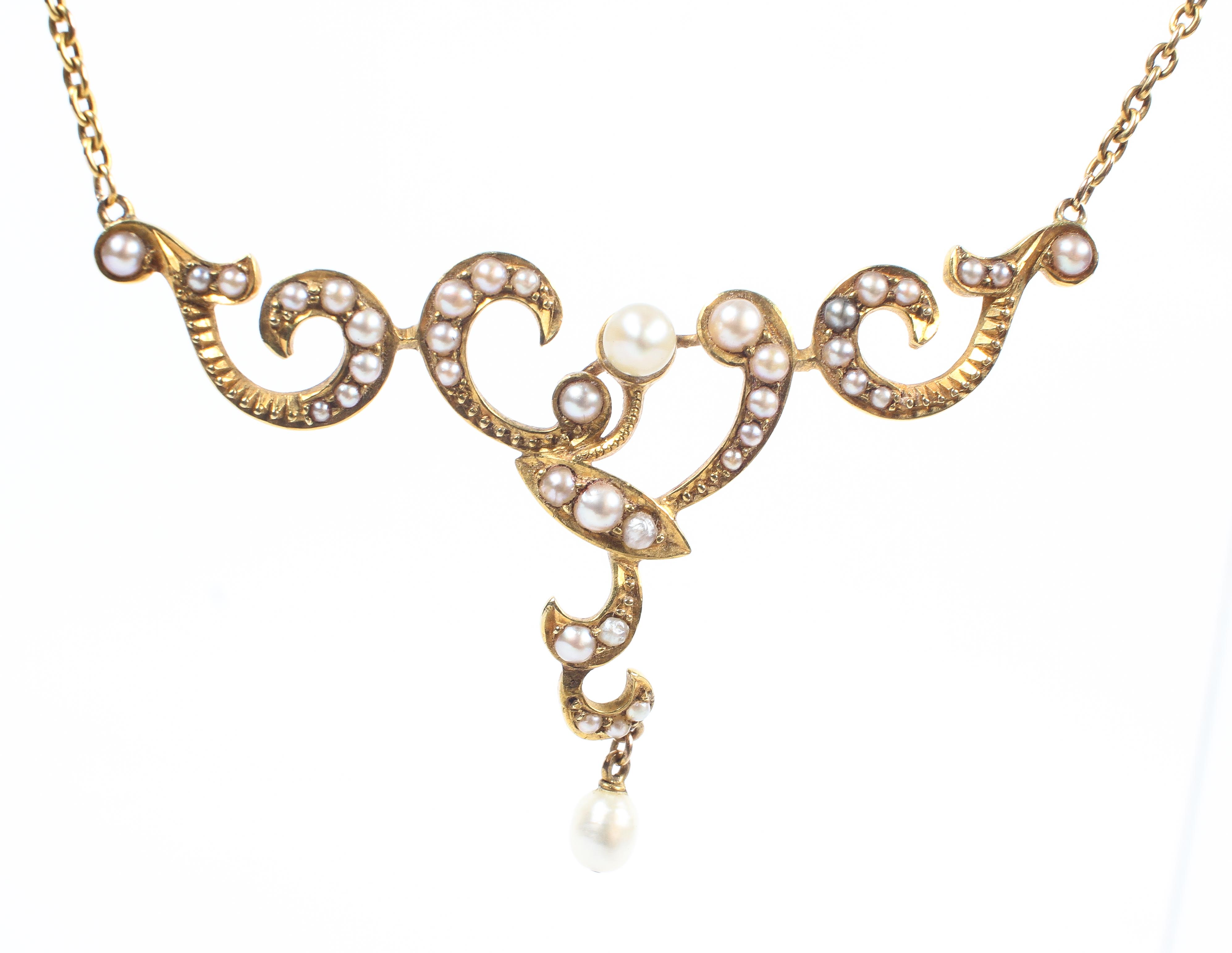 A yellow metal centrepiece necklace set with seed pearls and suspended from a trace link chain,