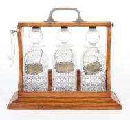 An Edwardian oak and white-metal mounted three bottle tantalus with later silver labels,