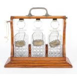 An Edwardian oak and white-metal mounted three bottle tantalus with later silver labels,