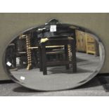 A mid century oval wall mirror, bevelled edge, the top mounted with metal shell motif,