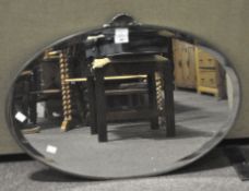 A mid century oval wall mirror, bevelled edge, the top mounted with metal shell motif,