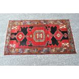 A vintage floor rug with a geometric pattern in shades of red, black and orange,