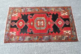 A vintage floor rug with a geometric pattern in shades of red, black and orange,