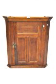 An early 20th century corner cupboard with two serpentine shelves behind a panelled door,