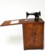 An oak cased Singer tredle sewing machine, with a fold over top and opening doors beneath,