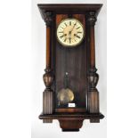 An Edwardian twin wooden cased Vienna style wall clock, complete with pediment,