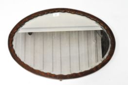 A early 20th Century bevelled edge oval mirror, with a wooden pie crust frame,