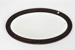 An oval oak framed bevelled edge mirror, the frame embellished with four round studs,