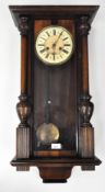 An Edwardian twin wooden cased Vienna style wall clock, complete with pediment,