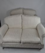 A pair of contemporary two seater sofas,upholstered in cream fabric, with scroll arms, on casters,