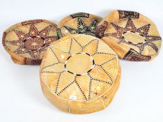 Four modern leather Moroccan pouffes in shades of brown and rust, embossed in gold, one stuffed,