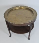 An Asian brass charger, on round wooden table, with lower shield,