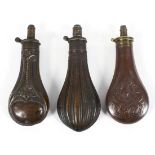 Three 19th century copper and brass powder flasks, one cast with pheasants in a cartouche,