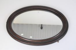 An oval mahogany framed mirror with carved details and bevelled edge,