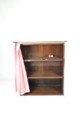 A mid-century mahogany waterfall bookcase with two shelves, fitted curtain pole and pink curtain,