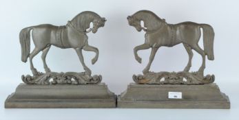 A pair of cast metal door stops or fire guards, modelled as horses, on rectangular bases,