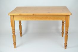 A contemporary pine kitchen table, rectangular with rounded corners, raised on turned wooden legs,