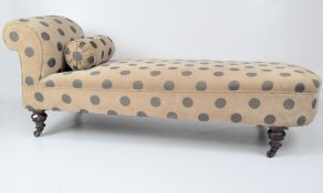 A Victorian chaise longue with matching bolster cushion, upholstered in beige with blue spots,