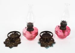 A pair of Victorian gilt-metal mounted cranberry glass wall mounted oil lamps,