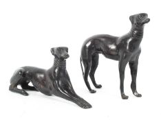 Two bronze models of greyhounds, both wearing collars, one standing, the other lying down,