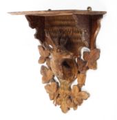 A Black Forest hanging wall shelf, carved with a suspended stag's head amongst leaves,