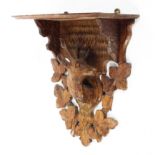 A Black Forest hanging wall shelf, carved with a suspended stag's head amongst leaves,