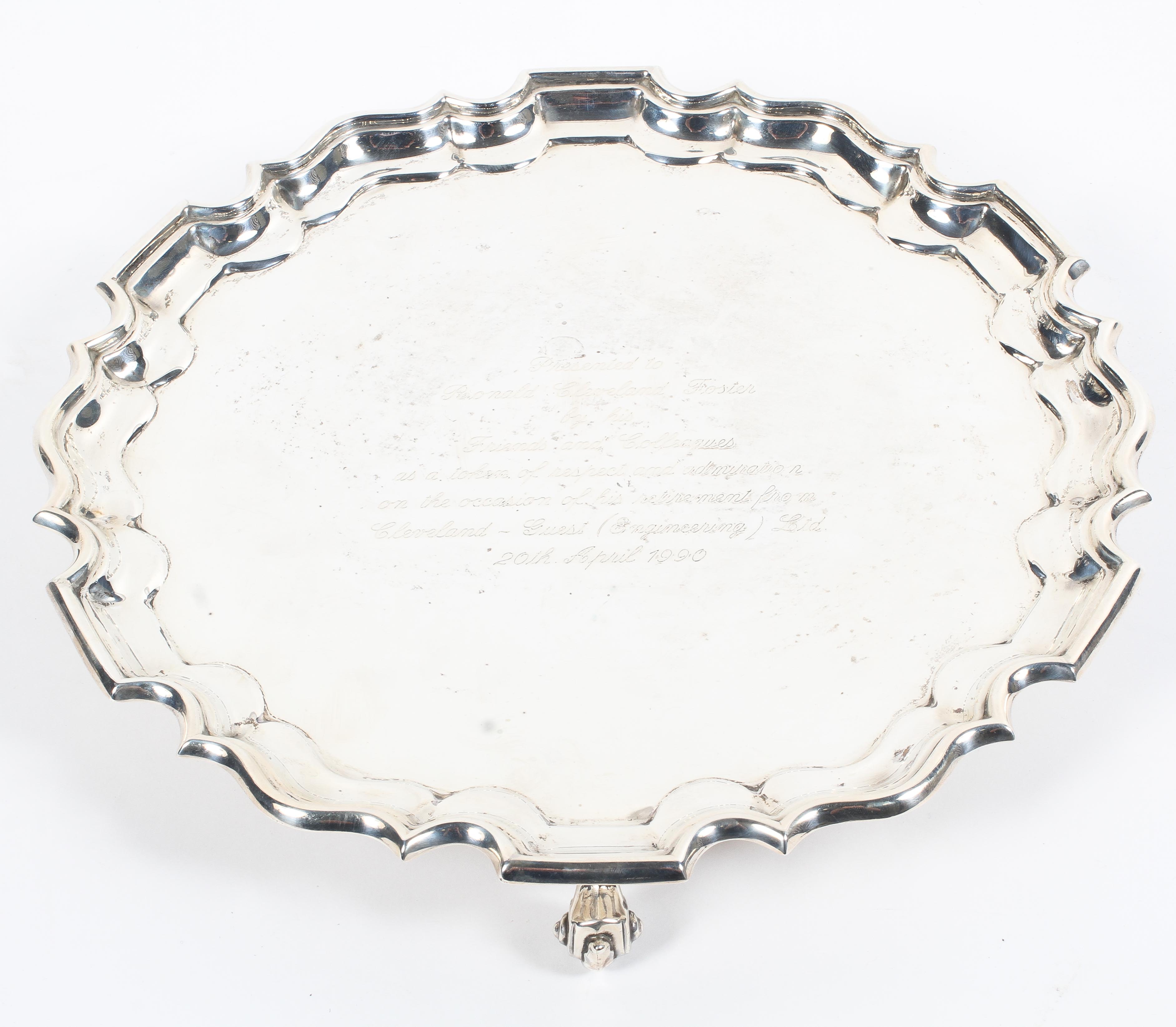 A sterling silver circular salver or card tray with pie crust border raised on three scrolling feet.