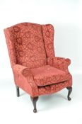 A vintage wing back chair on cabriole legs, with red, leaf-patterned upholstery,