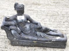 A concrete stone garden ornament of a woman seated on a chaise lounge,