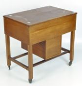 A 1960's teak work table with hinged cover, on wheels,