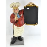 A model of a chef in traditional uniform holding a blank menu,