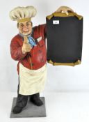 A model of a chef in traditional uniform holding a blank menu,