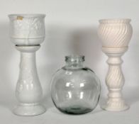 Two white ceramic jardiniere stands and a glass carboy,