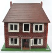 A vintage dolls house painted as red brick with white window frames, on a green base,