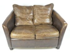 A vintage two seat brown leather sofa, raised upon tapering wooden feet,