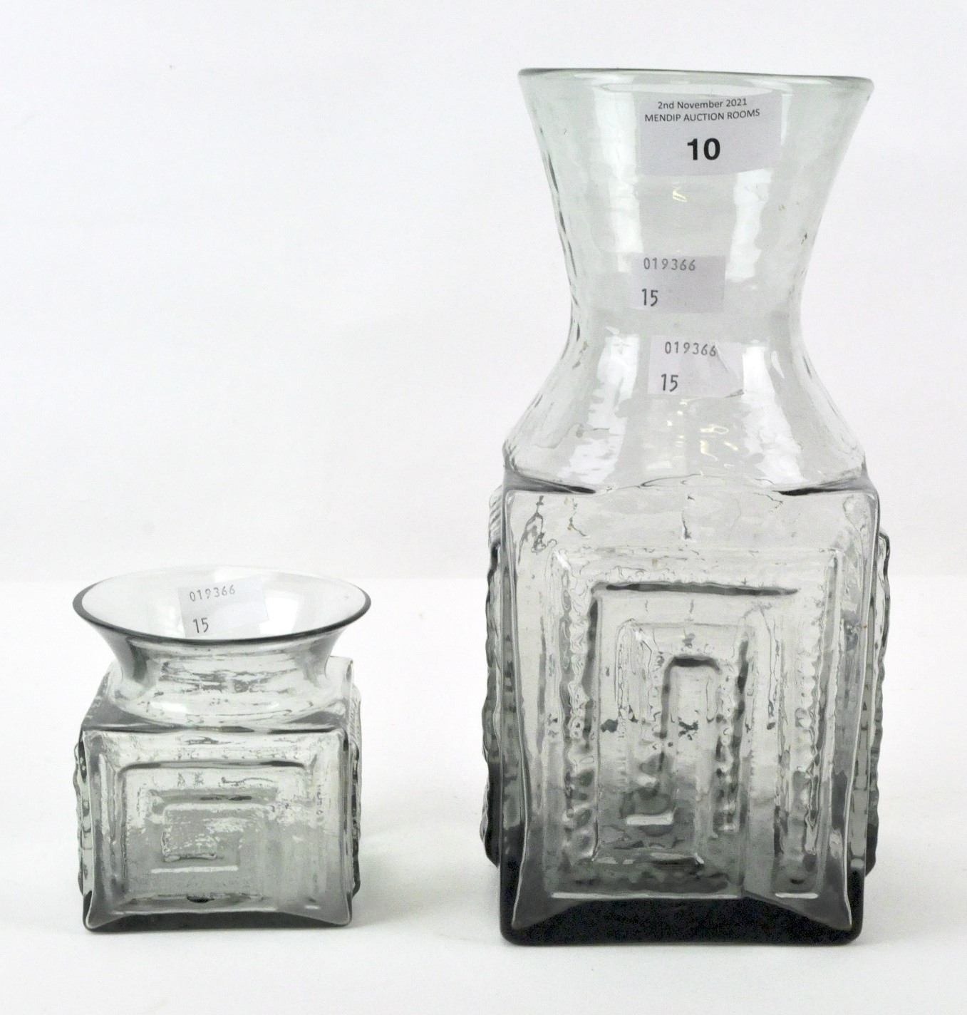 Two mid-century smoky grey Dartington glass vases of square body with raised meander pattern,