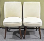 A pair of modern upholstered chairs, covered in a beige fabric, raised upon tapering feet,