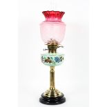 An Edwardian brass-mounted oil lamp with cranberry glass shade,