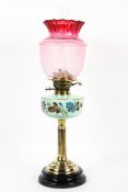 An Edwardian brass-mounted oil lamp with cranberry glass shade,