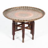 A Middle Eastern copper charger table, the large top engraved with panels of figures,
